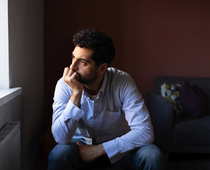 Imagem de um homem sentado, olhando para fora da janela com uma expressão de preocupação e nervosísmo
