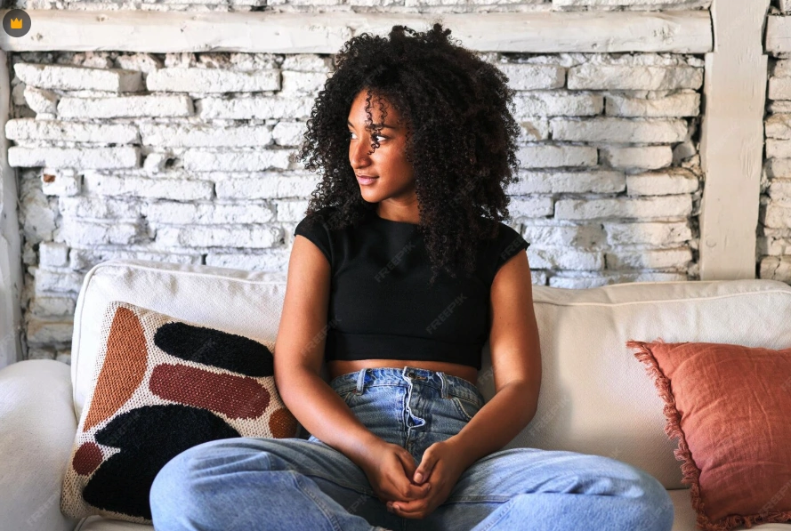 Imagem de uma mulher sorridente sentada no sofá, olhando para o exterior através de uma janela